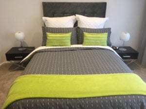 Charcoal coloured headboard. Bed has grey duvet with lime coloured throw.